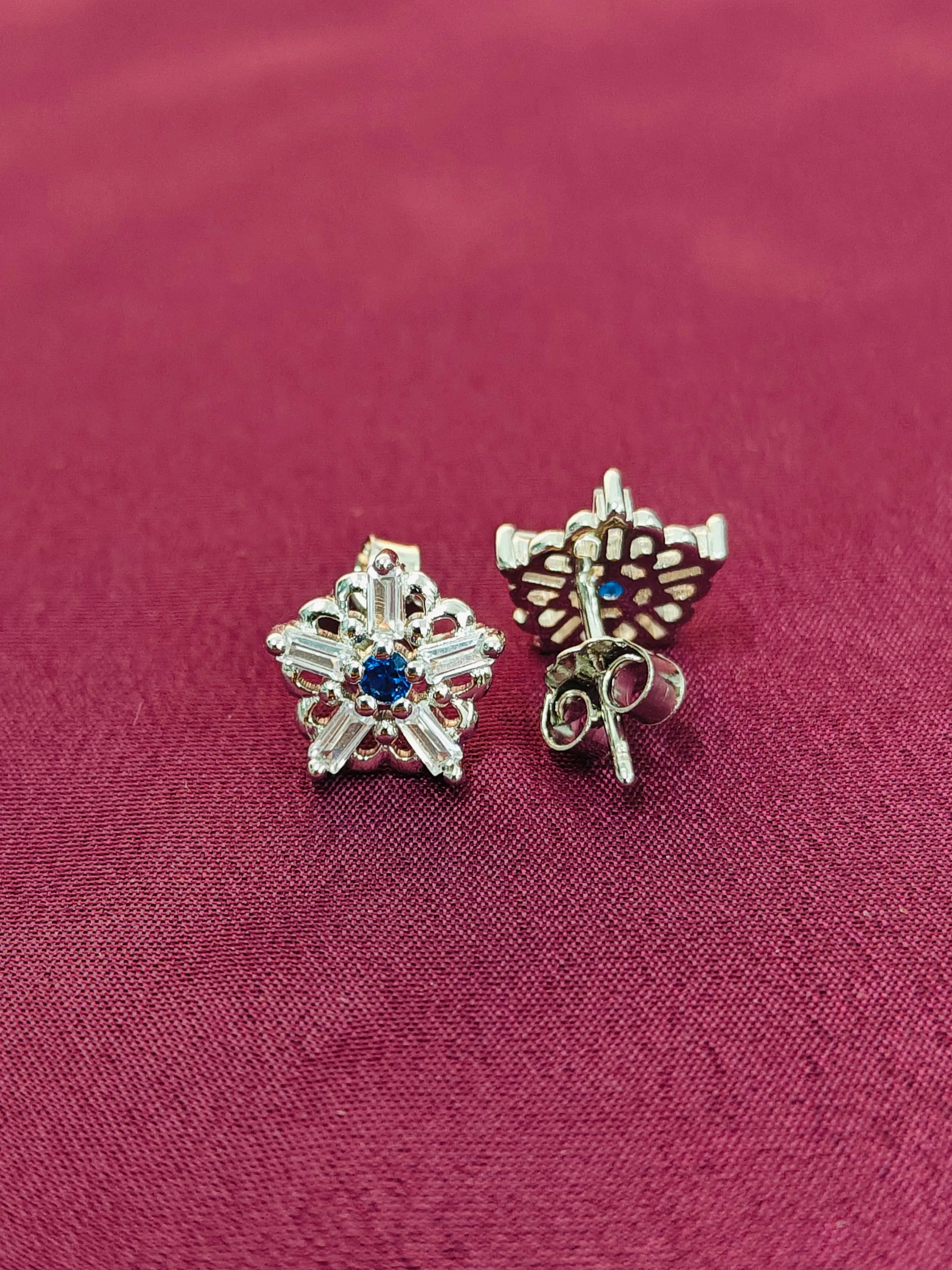 Two silver star-shaped earrings with blue stones on a red fabric background